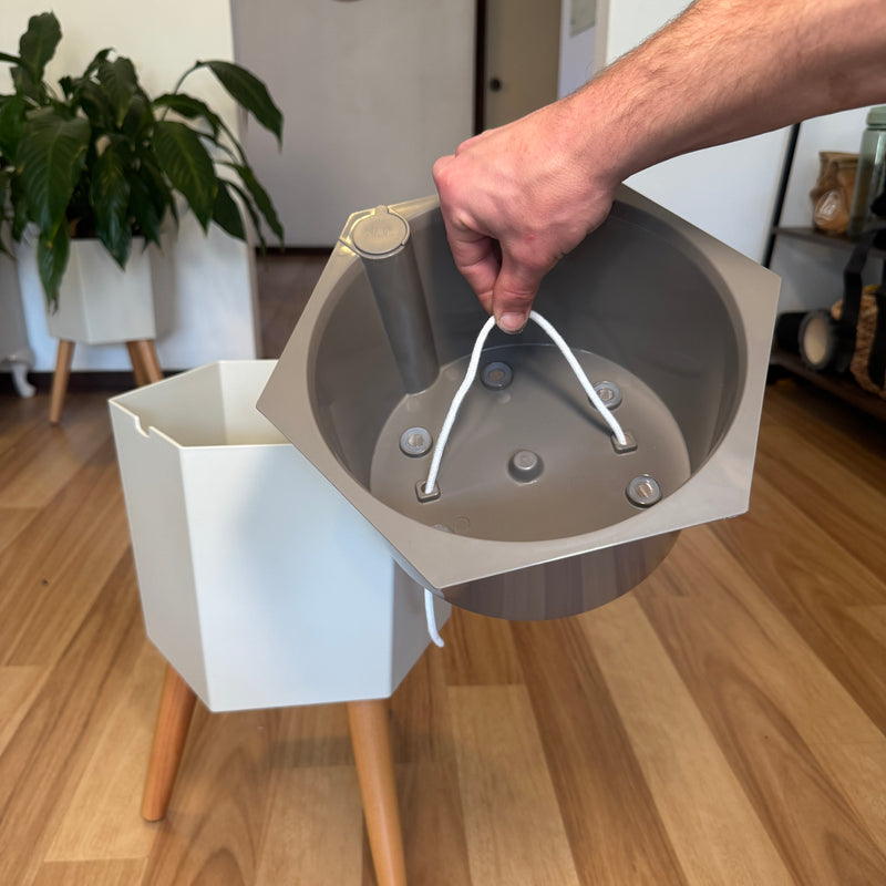 A hand lifting the inner pot clear of the planter, the cotton wick threaded through its base